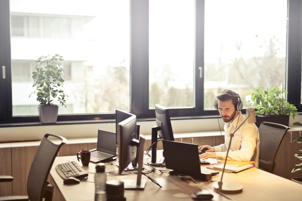 pexels-photo-845451-845451 A businessman sits at a desk using multiple computers and a headset in a well-lit modern office.